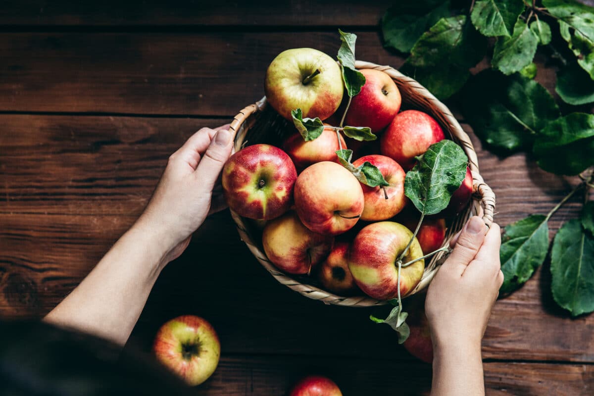 Woman with a basket of apples on a table.